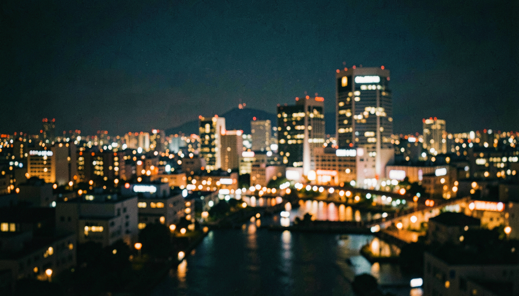 梅田の夜景に浮かぶ温かみのある灯り、深い青と金色が調和する都会的で落ち着いた雰囲気の広角風景。